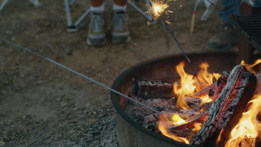 People are having a cook out and they are lighting sparklers from the flames
