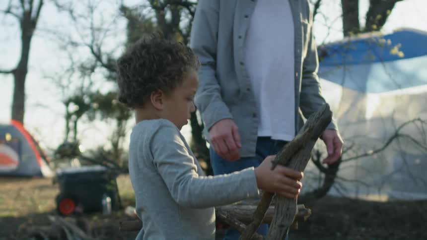 Boy helps father carrying wood for a campfire in the countryside
