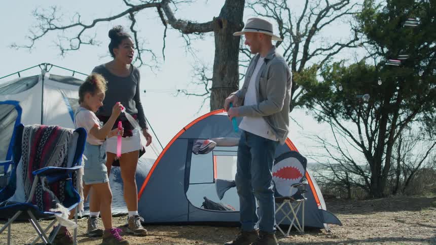 A family laughs while playing with a bubble wand at their campsite