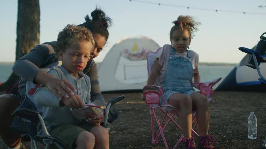 A woman helps her son light a match to toss onto a campfire