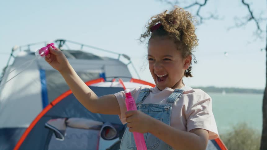 A girl waves around a bubble wand while camping