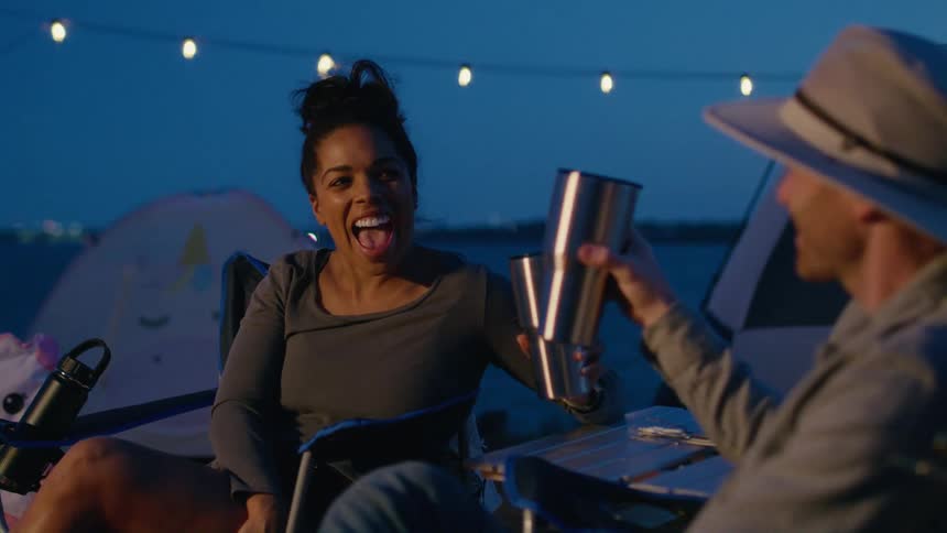 Young happy couple sitting outdoors toast while camping at evening
