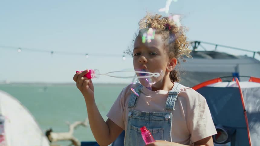 Girl playing with soap bubbles on a campsite near the coast