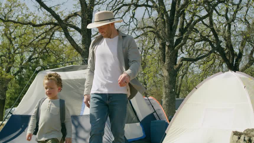 A man talks to a child as they walk together across a campsite during the day
