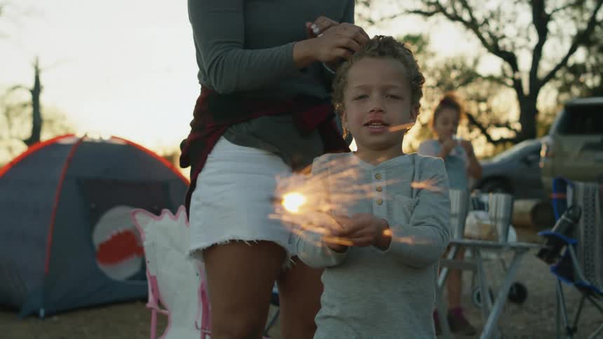 Boy standing next to his mother playing with a sparkler wile camping at sunset