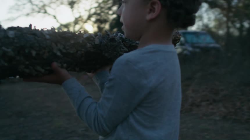 Child carries log while walking into campsite