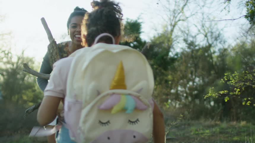 A little girl wearing a backpack is collecting firewood with her mother
