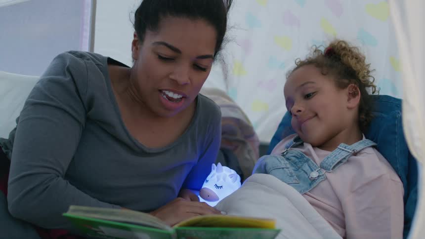 A woman is in a tent reading a book to her young daughter