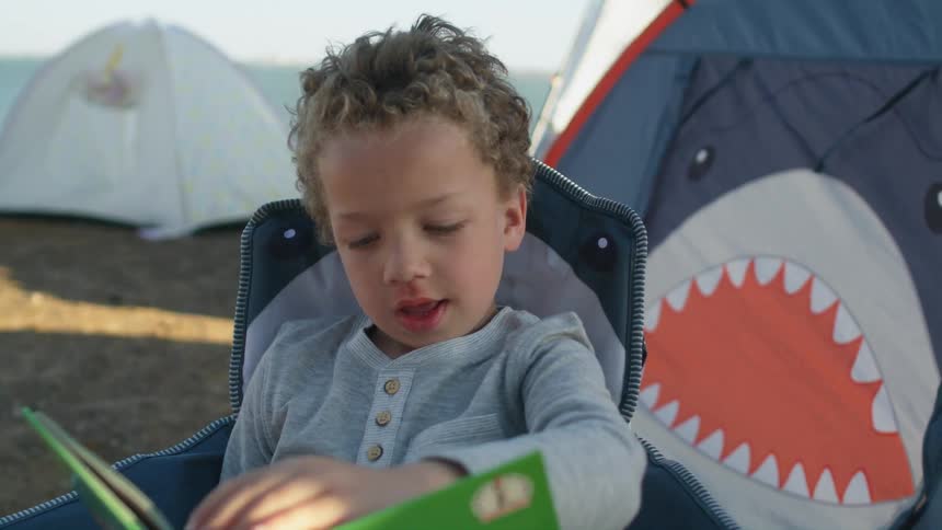 A young boy camping reads a book