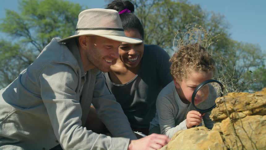 Mom and dad smile as they help their little boy look for bugs through a magnifying glass