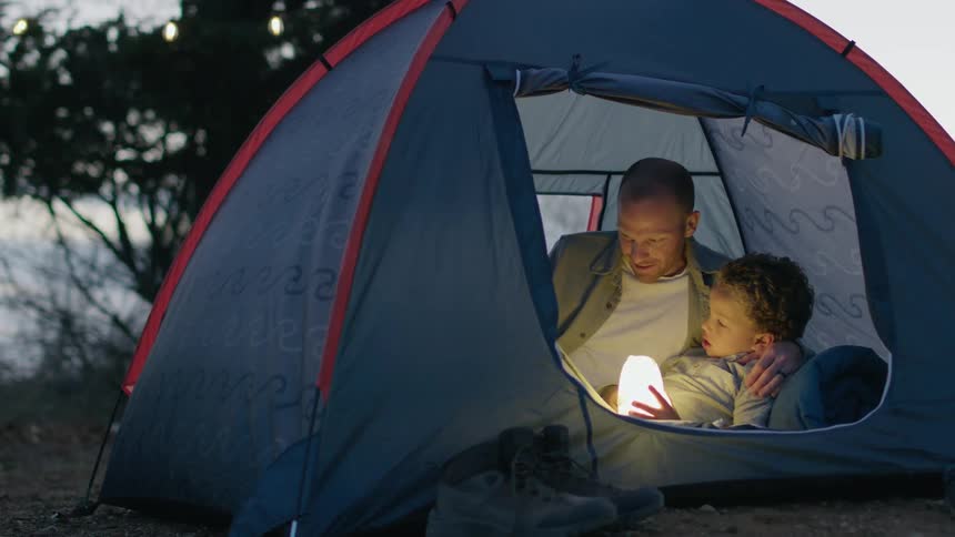 A man and his son are in a tent reading a book