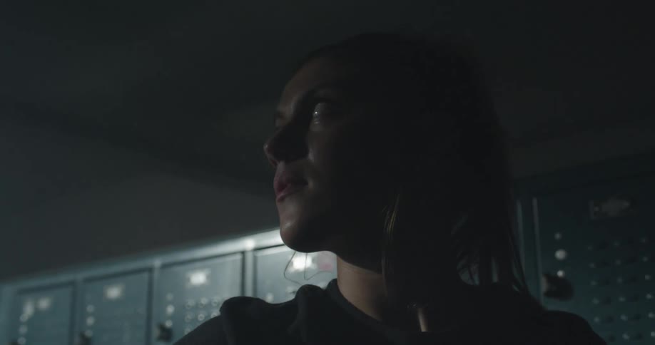 A woman stands in a dark locker room