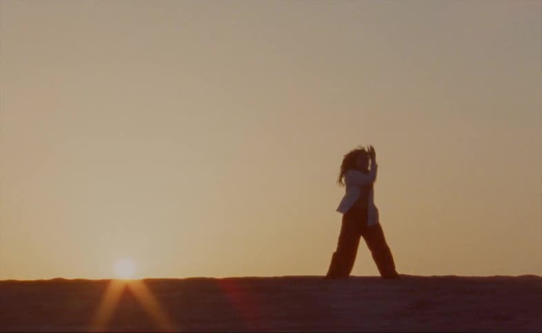 A woman dances hip hop style in an open field at dusk