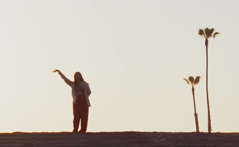 Female dancer dances outdoors back lit by sunlight from the horizon