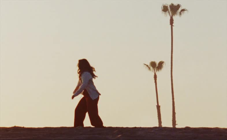 Female dancer dances on sandy ground near two palm trees