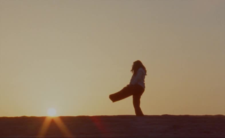 Female dancers dances back lit by sun sitting on the horizon