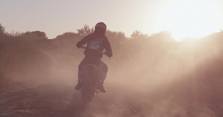 A dirt bike rider makes a turn at sunset and drives forward on a trail
