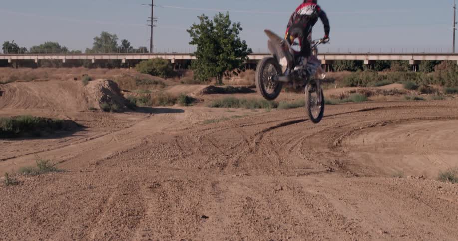 A dirt bike rider comes down from a high jump in the dirt