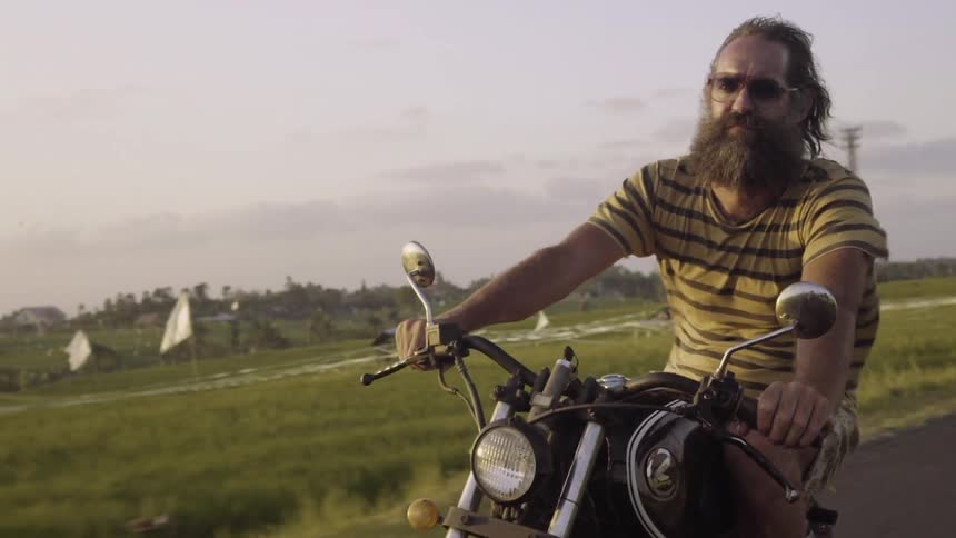 A man wearing a t-shirt and shorts rides a motorcycle