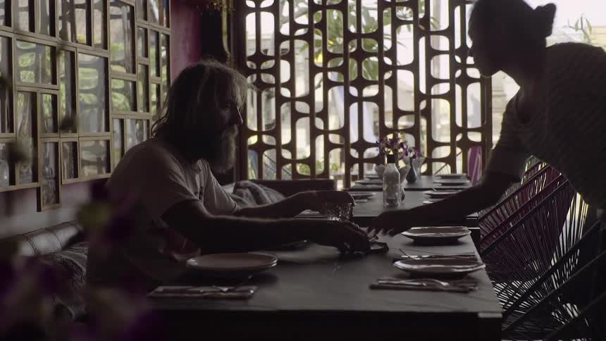 A bearded man sits at a table in a restaurant