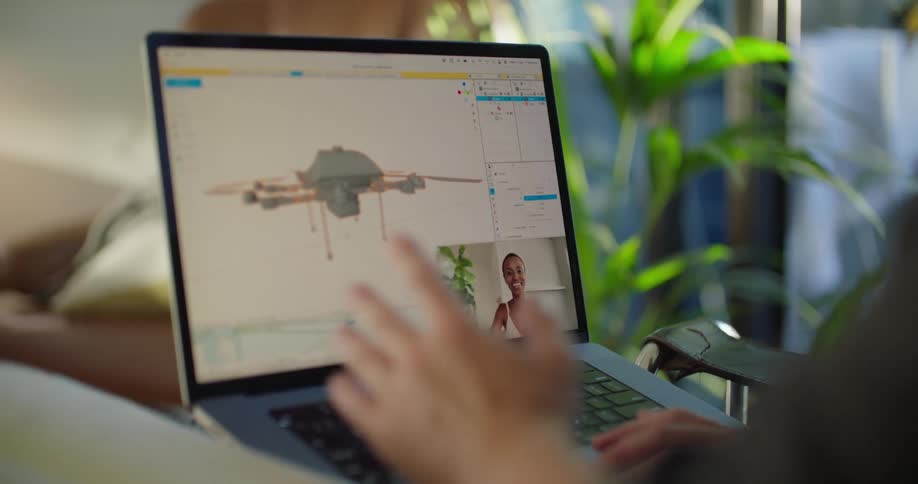 A man is working with three dimensional software on a laptop computer as he video chats with a woman