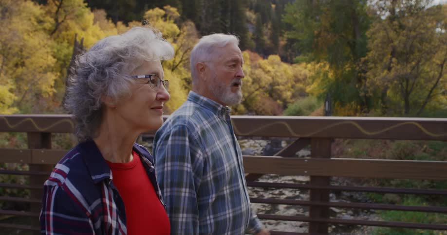 An elderly man and woman walk across a bridge crossing a river
