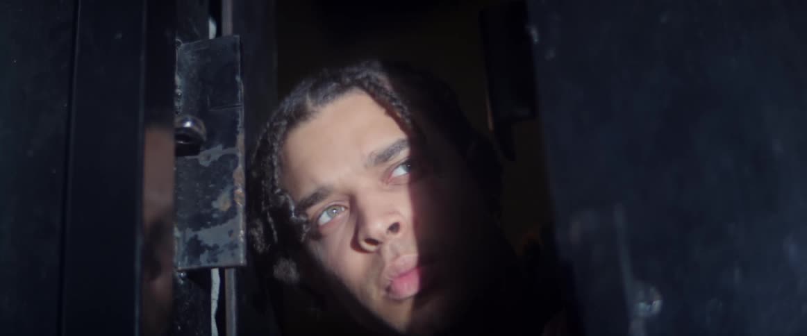 A young man pokes his head out a doorway and cautiously looks out