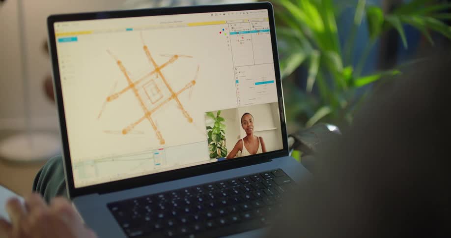A man video chats with a coworker on his laptop as he works on a design