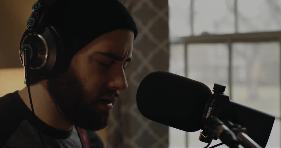 Young bearded man singing into a microphone near a window at home