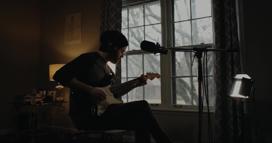 Silhouette of a young man playing guitar near a window at home