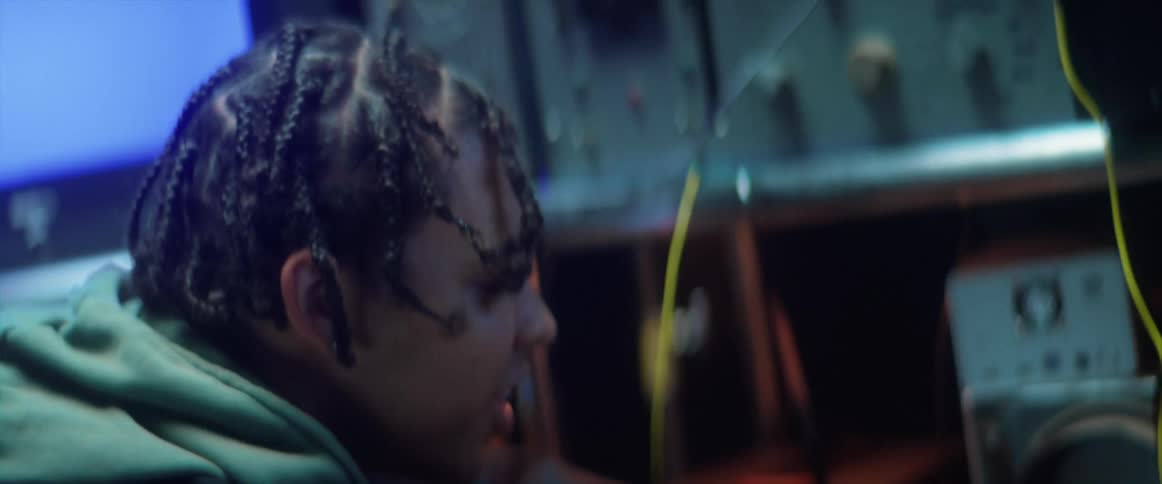 A black teenage boy is standing near electronic equipment as static flashes on television screens he is looking around and touching dials