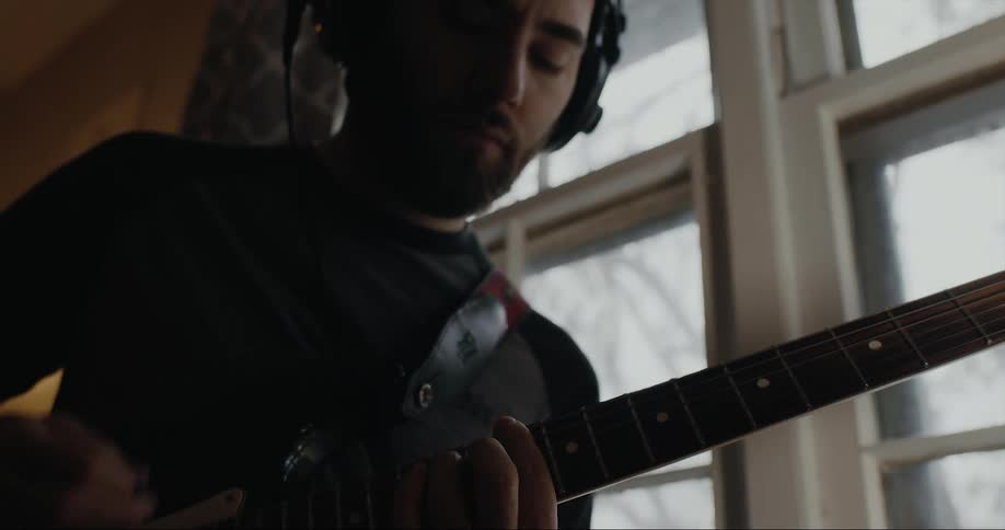 Young man wearing headphones strumming an electric guitar on a room at home