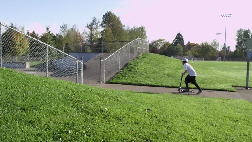 Two kids skate into a park on a sunny day