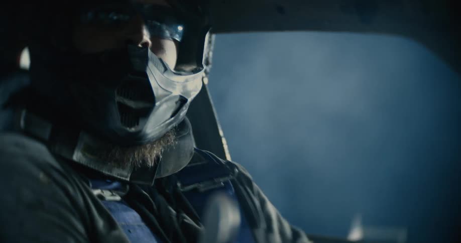 The driver of a demolition derby car is wearing a helmet and goggles as he navigates his automobile