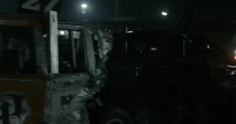 A demolition derby car is driven past other wrecks behind a stadium