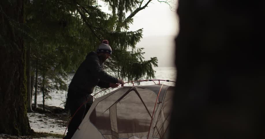 A man is assembling a tent by the water