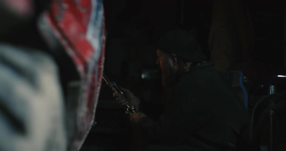 A man wearing protective gear is using a welding torch to weld something on a beat up car