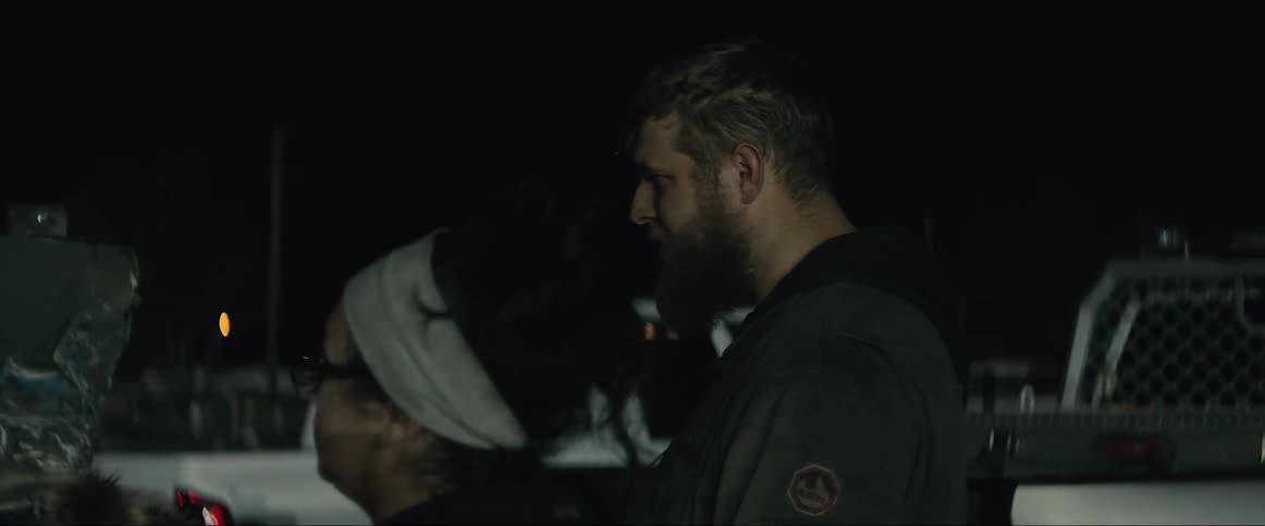 Man and woman talks as a third man examines damaged car using a handheld light at night