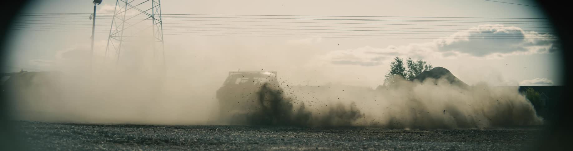 A demolition derby car kicks up dust and dirt as it spins around in gravel