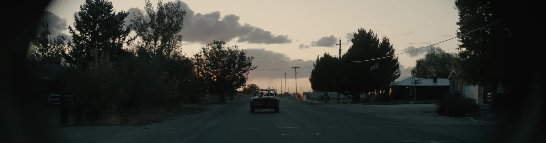 An automobile is traveling on a neighborhood street passing houses and trees