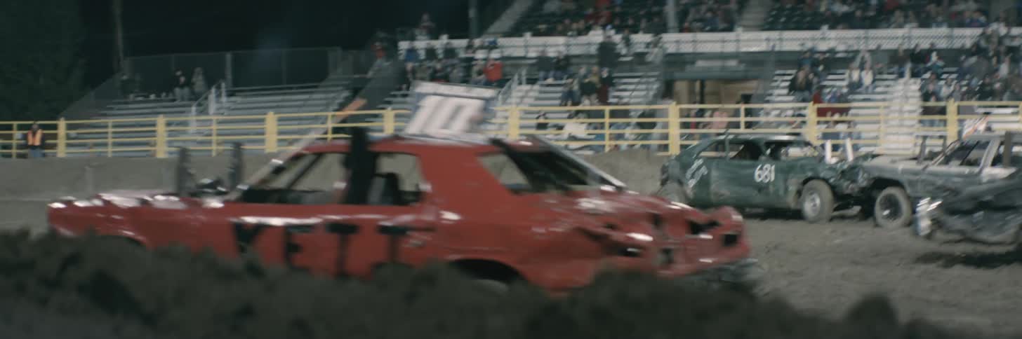 Drivers are in a dirt ring smashing their cars into each other as an audience watches