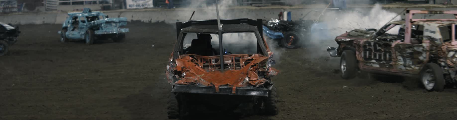 Smashed cars in a demolition derby are smoking and moving on wobbly wheels