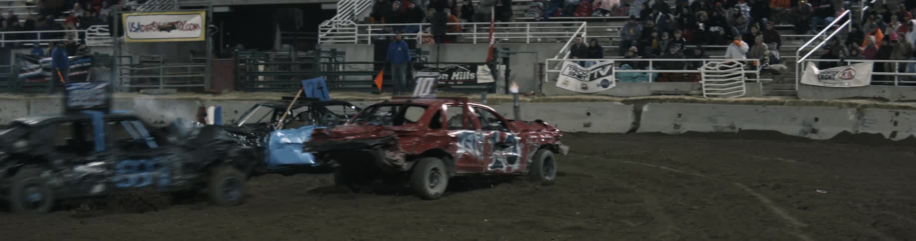 A red car travels across the dirt stadium only to be pushed into the wall during a demolition derby