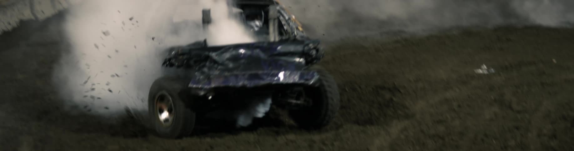 A smashed automobile is smoking as it moves in a demolition derby and it crashes into another car