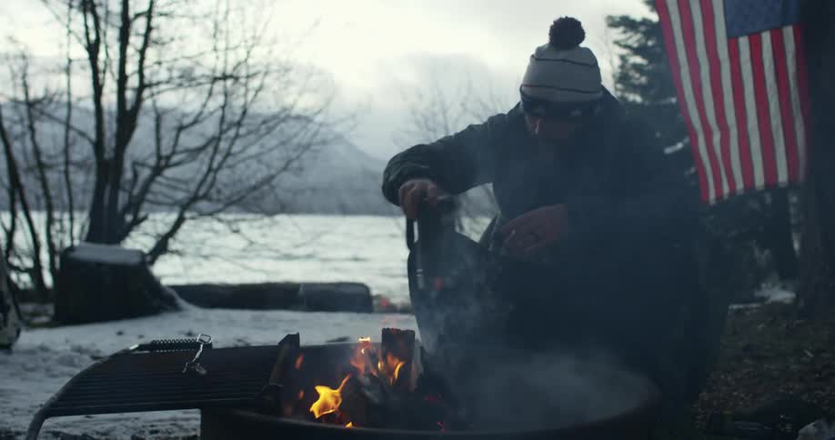 Man warms himself by fire with hot drink
