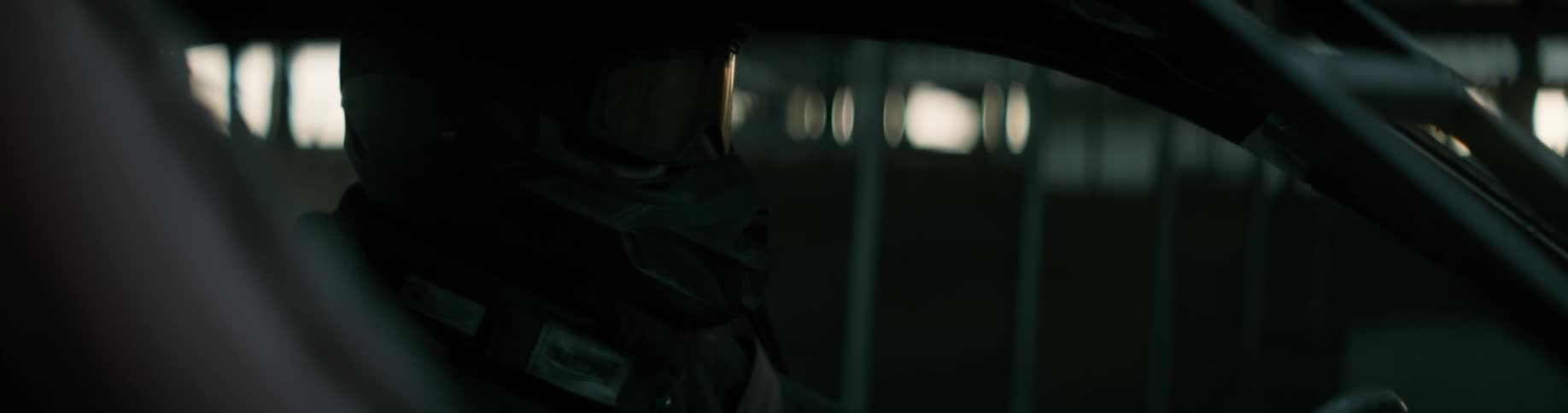 A man is sitting in the dark inside a vehicle wearing a helmet