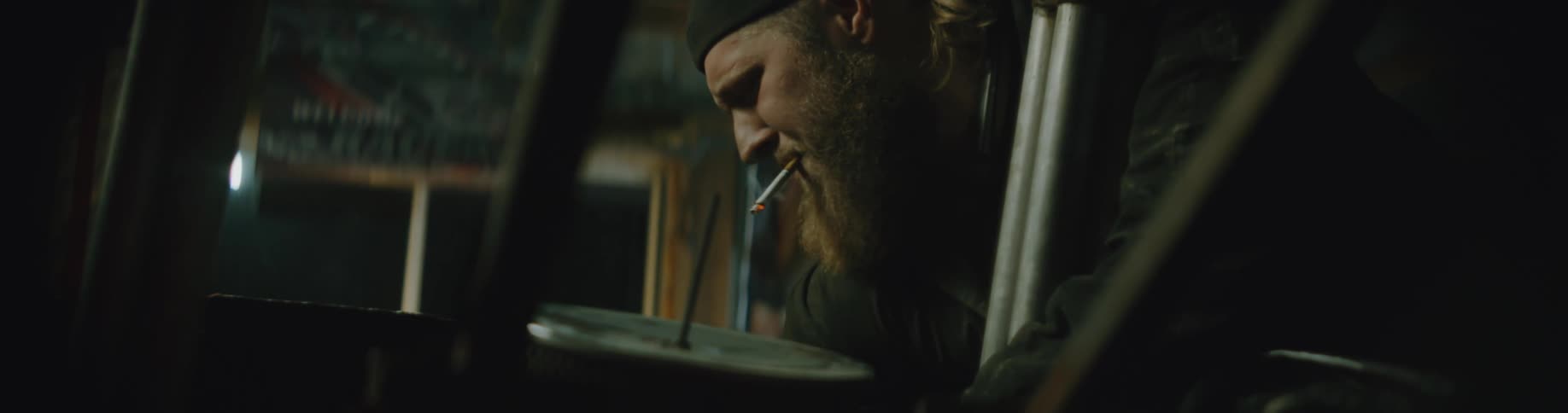 Man wearing overalls smokes while examining derby car reinforced with metal pipes