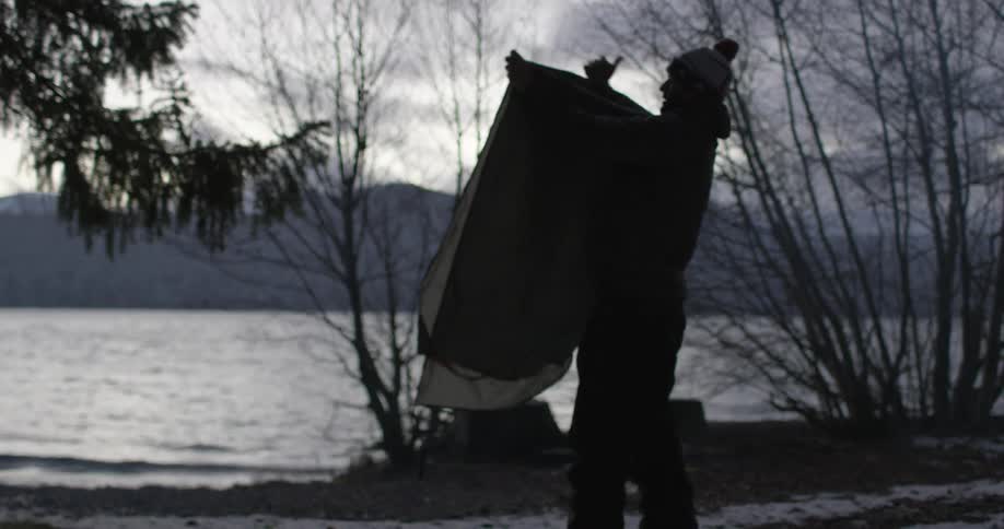 A man folds up a blanket by the water