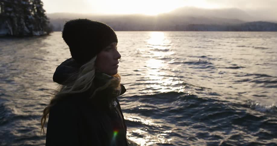 A woman is standing close to some rough waters at sunset