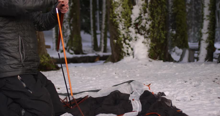 A man is setting up a tent in the snow